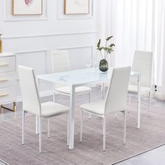 a white dining table with four chairs and a vase on the top, in a living room