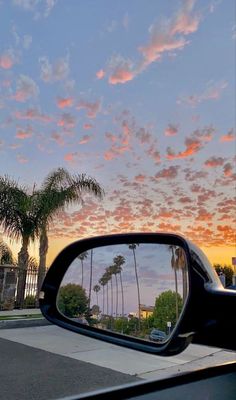 palm trees are reflected in the rear view mirror of a car as the sun sets