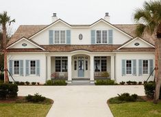 a large white house with blue shutters and palm trees in front of the door