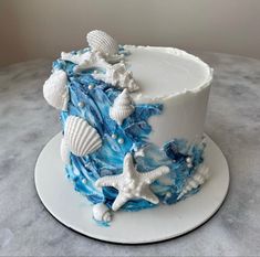 a blue and white cake with sea shells on it's side, sitting on a table