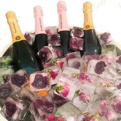 several bottles of champagne and ice cubes in a bowl with flowers on them,