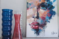 two vases and a painting on a shelf next to each other, one with a woman's face painted on it