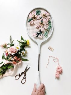 a person is holding a flower shaped object with scissors and flowers on the table next to it