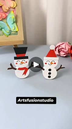 two snowmen are standing next to each other in front of a painting and flowers