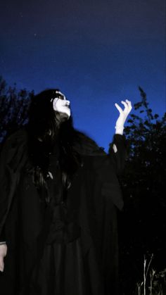 a woman dressed in black is holding her hands up to the sky while wearing a mask