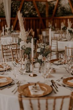 the table is set with white linens, gold chargers and tall centerpieces