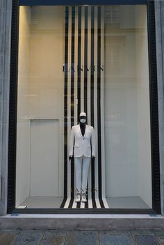 a mannequin dressed in a white suit and black tie stands behind a window display