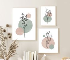 three framed art prints on the wall above a shelf with books and plants in vases