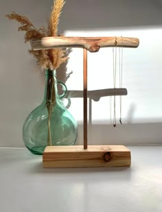 a green glass vase sitting on top of a wooden stand next to a small plant