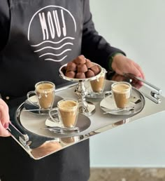 a person holding a tray with coffee and chocolates on it