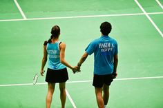 two people standing on a tennis court holding hands