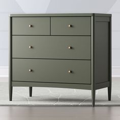 a green chest of drawers with gold knobs on the top and bottom, in front of a white wall