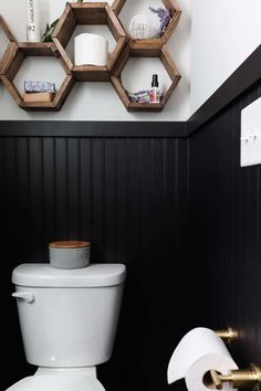 a white toilet sitting in a bathroom next to a wooden shelf filled with toilet paper