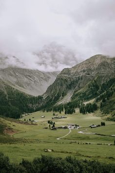 the mountains are covered in green grass and trees, while clouds hover over them