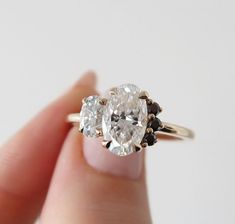 a woman's hand holding an oval shaped diamond and two smaller round diamonds on it