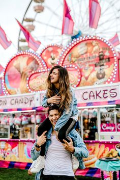 a man carrying a woman on his back in front of a carnival ride at an amusement park