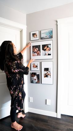 a woman standing in front of a wall with pictures on it and holding her hand up to the wall