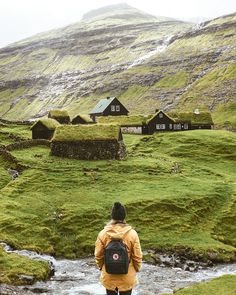 a person with a backpack is standing in the middle of a stream and some houses