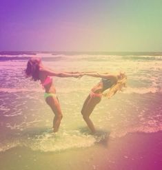 two young women are playing in the water at the beach while one holds her arm out