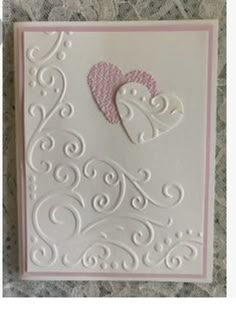 a white and pink card with a heart on the front, sitting on a lace tablecloth