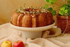 a bundt cake sitting on top of a white plate next to an apple and green plant