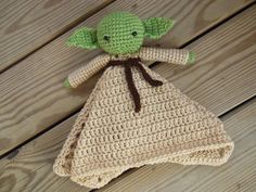 a crocheted baby yoda doll laying on top of a wooden floor next to a blanket