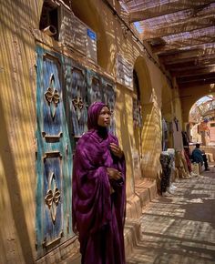 a woman standing in front of a building wearing a purple shawl and head scarf