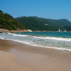 people are swimming in the ocean on a beach with hills in the background and blue sky