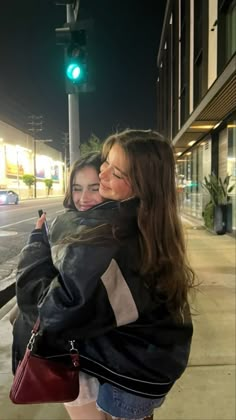 two girls hugging each other on the street corner at night with green traffic lights in the background