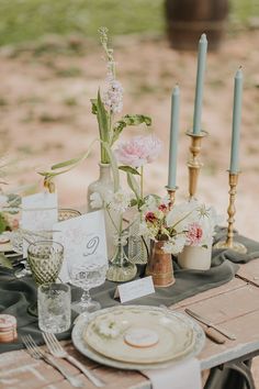 an outdoor table set with flowers and candles