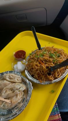 two plates of food on a yellow tray in the back seat of a car, with chopsticks and sauce