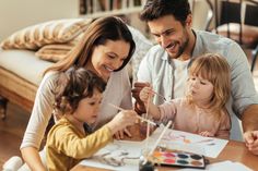 a man and two children are painting with their mother at the table in front of them