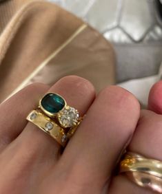 a close up of a person's hand holding a ring with an emerald and diamond