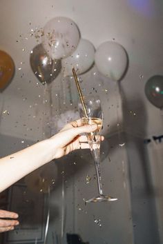 a person holding a wine glass in front of balloons and confetti on the wall