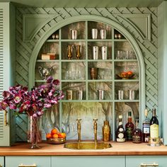 a kitchen with green cabinets and an arched glass door over the sink is filled with liquor bottles