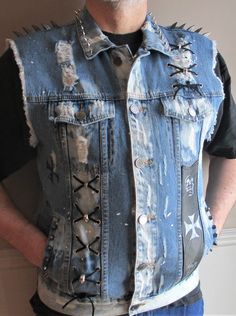 Faded blue jean vest with black leather insert and back panel and TONS of metal spikes A total of 25 silver metal tree spikes edge the entire collar A row of Gunmetal Dragon Spikes sit atop each shoulder Leather laced through silver metal grommets and accented with silver skulls decorate the vest front The Black leather panel on the vest front is painted with skulls and a cross in silver metallic Both front pockets are edged with silver mushroom spikes The back center panel has black leather with a skull collage painted in silver metallic 3 silver mushroom spikes decorate the top of the leather back panel A Cross pattern has been painted in black metallic on the back side panel This is a mans size XL Carbon brand vest with front button closure, 2 lower pockets, 2 upper pockets Spot clean o Distressed Punk Denim Vest For Streetwear, Punk Distressed Denim Vest For Streetwear, Jean Jacket Vest Outfits, Punk Leather Jacket, Blue Jean Vest, Vest Outfits Men, Jean Jacket Vest, Studs And Spikes, Metal Spikes