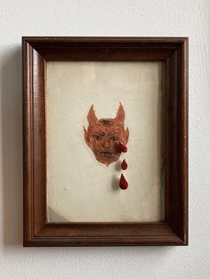 a framed drawing of a demon with blood dripping from it's mouth on a white wall