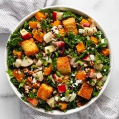 a white bowl filled with salad on top of a marble counter next to a blue towel