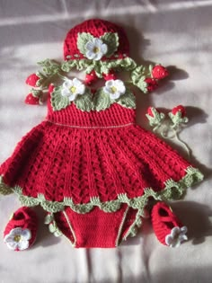 a crocheted red dress and matching hat is laying on a white sheet with flowers