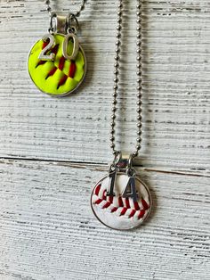 two necklaces that have different designs on them, one has a baseball ball and the other has a letter