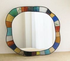 a colorful mirror sitting on top of a counter next to a white wall and window