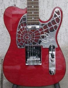 a red guitar with spider webs on it's body and neck, sitting in front of a white wall