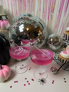 some pink cocktails are sitting on a table with disco balls and cupcakes