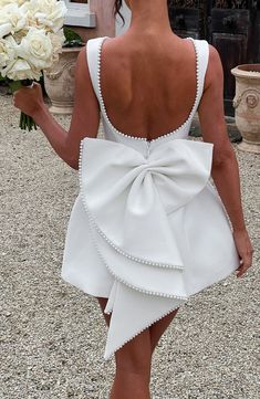 the back of a woman in a white dress holding flowers