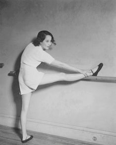 an old photo of a woman stretching her legs on a rail in a room with wood floors