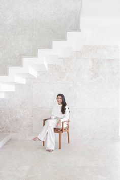 a woman sitting on a chair in front of a stair case with white marble walls