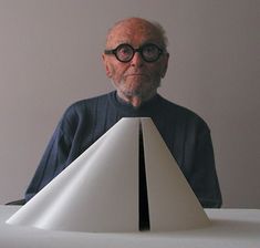 an old man sitting at a table with a paper boat on it's head