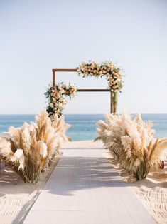 an outdoor ceremony setup with pamodia and flowers on the aisle at the beach