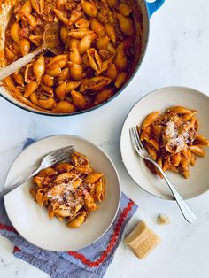 two plates with pasta and cheese on them next to a pot of meaty sauce