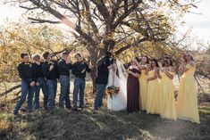 a group of people standing next to each other in front of a tree with their hands up